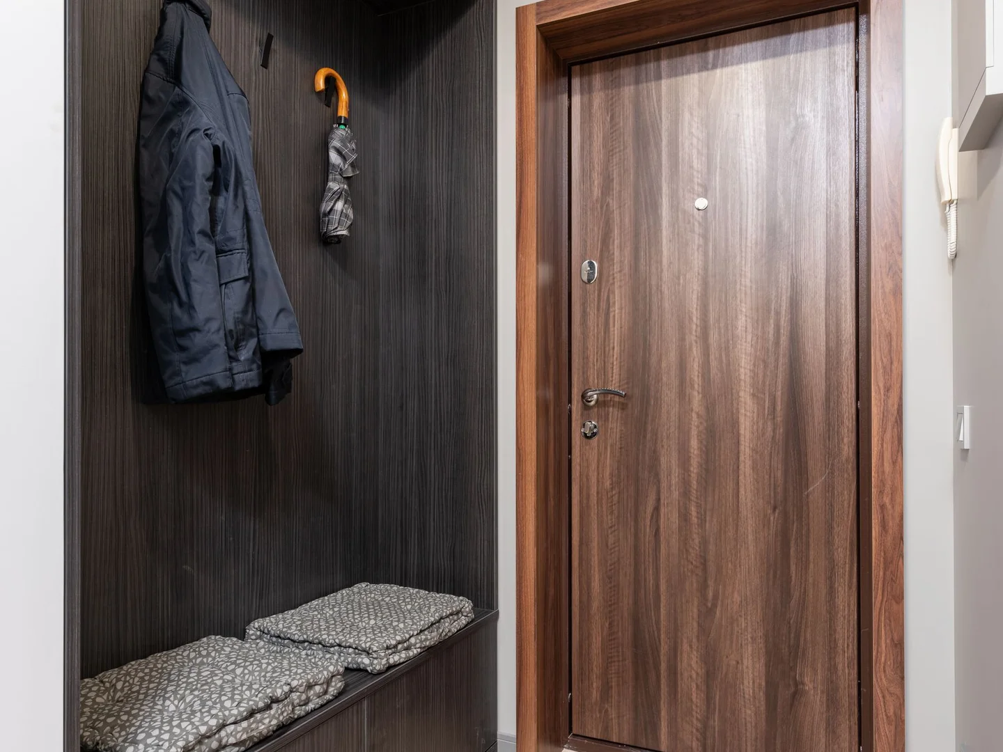 Coats, shoes and a bench arranged beside an entry door.