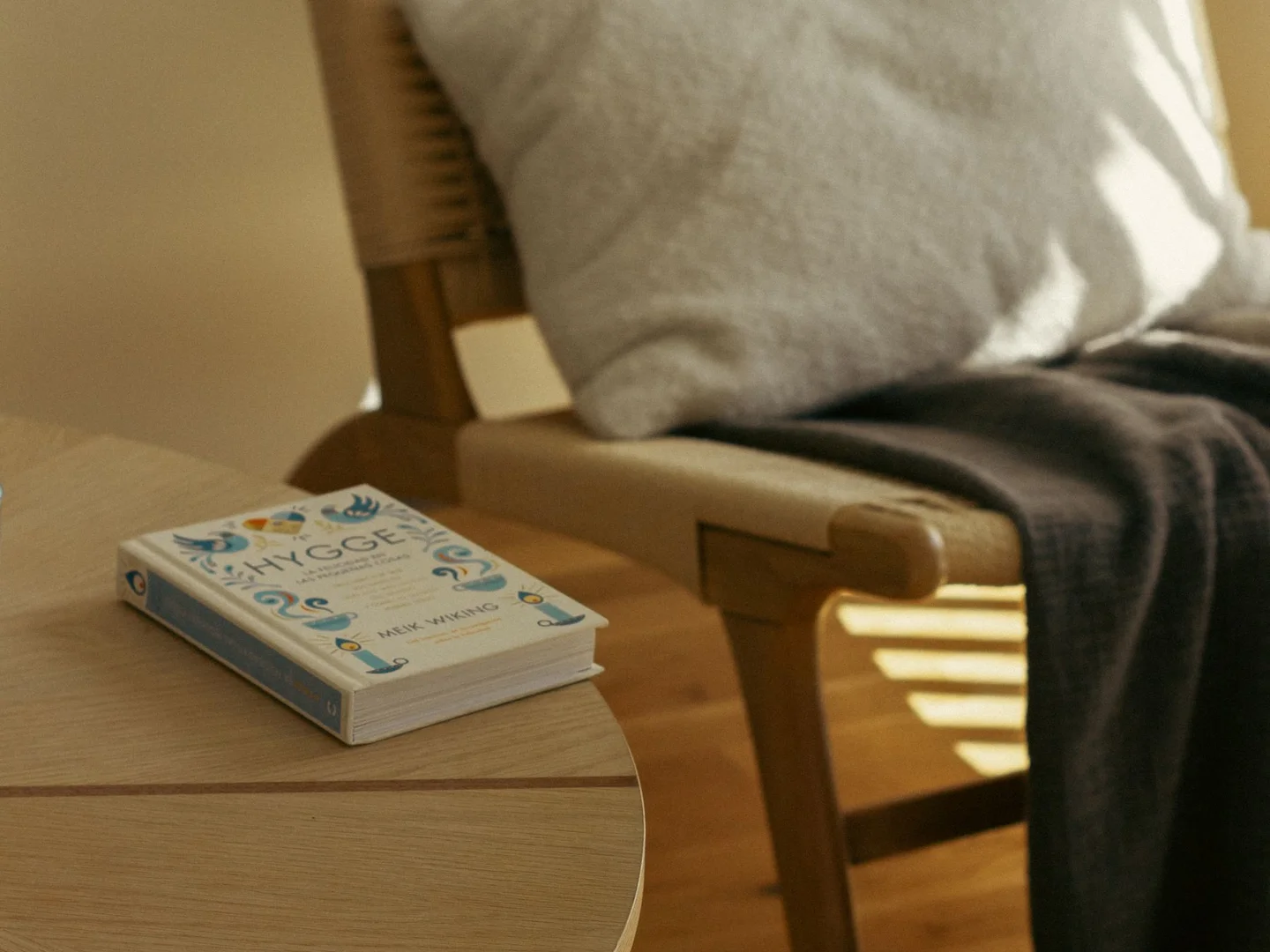 A chair with a cushion and blanket beside a small table and book.