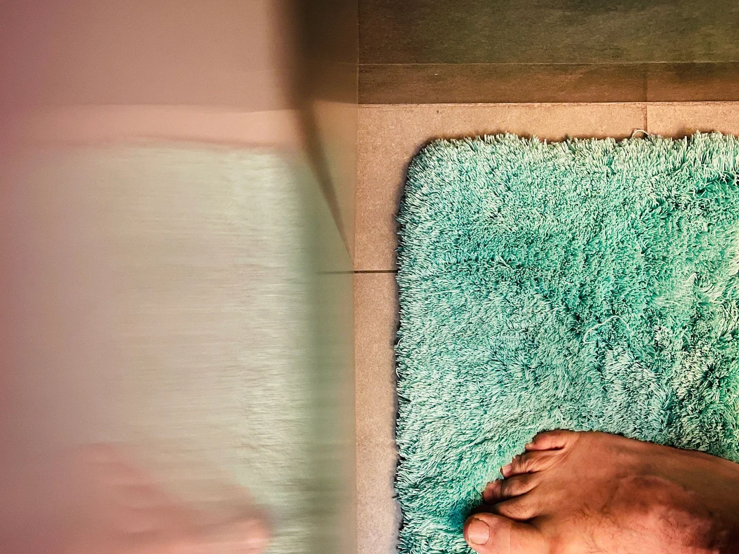 A green bath mat on a tiled bathroom floor.