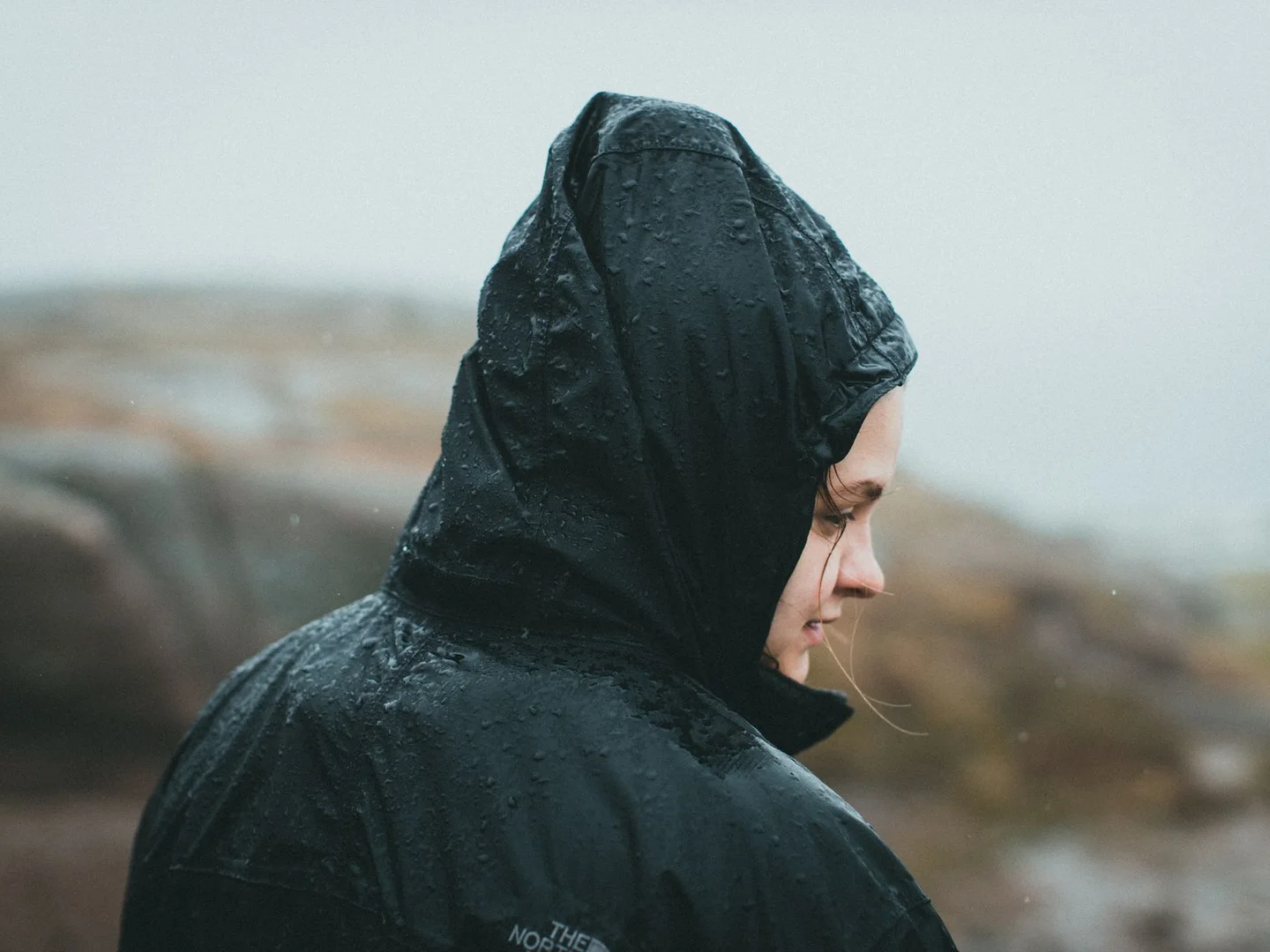 A woman wearing a hooded rain jacket outdoors.