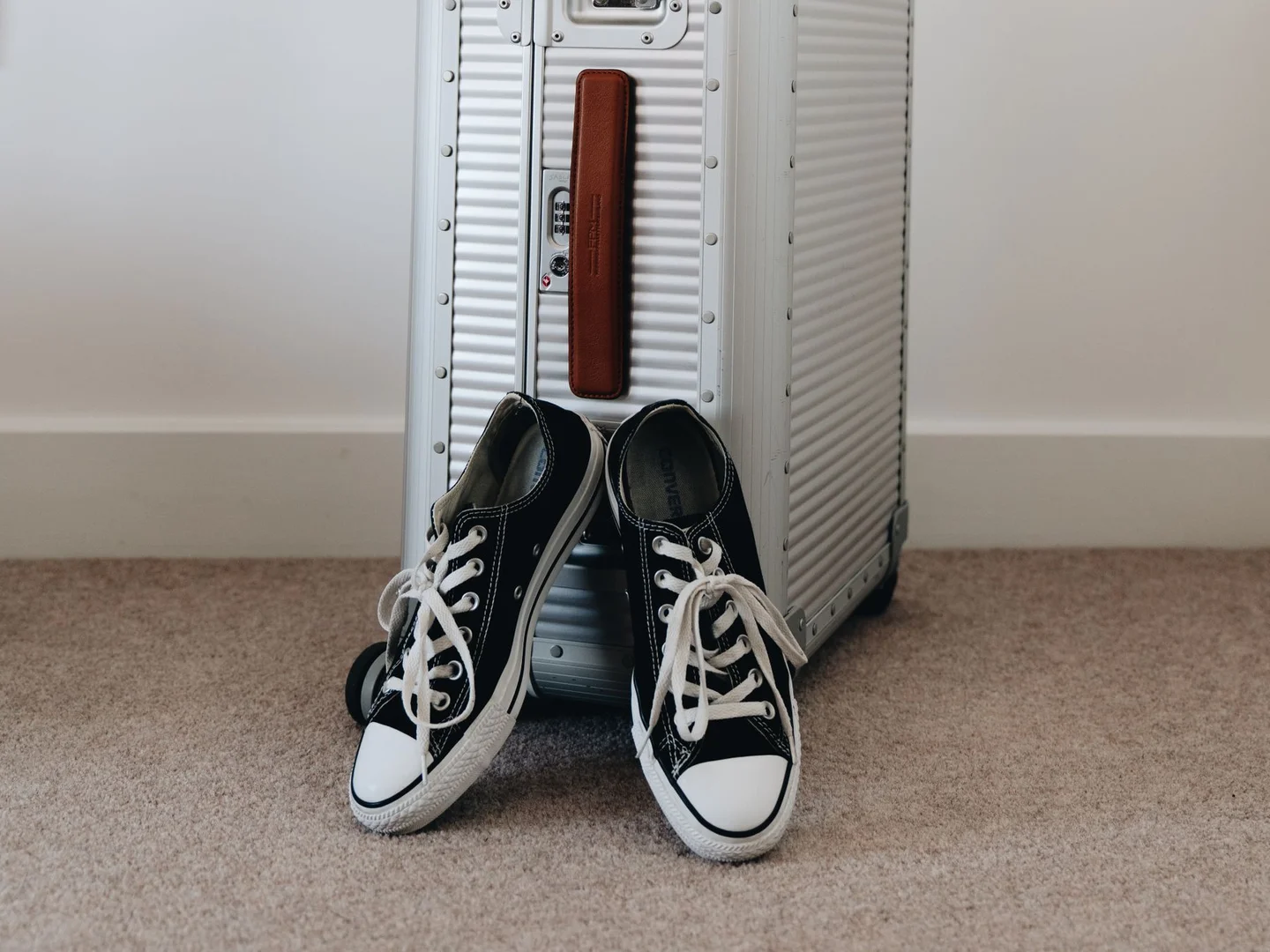 A pair of canvas sneakers beside a suitcase.