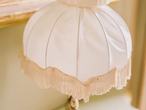 A white lampshade finished with decorative fringe.