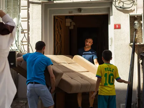 People carrying a wrapped sofa through a building entrance.