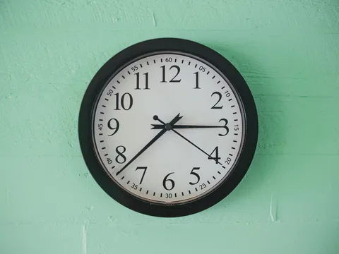 A round black-framed wall clock against a pale green wall.