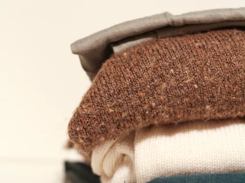 A stack of folded sweaters showing their knit textures.